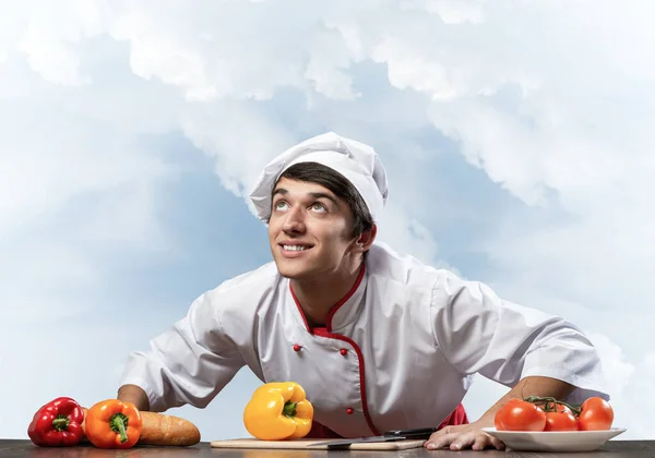 Joven chef sonriente de pie cerca de la mesa de cocina —  Fotos de Stock