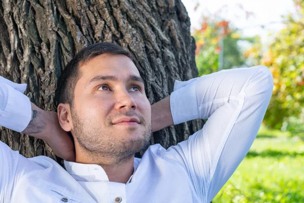 Młody człowiek siedzi pod drzewem w słoneczny dzień — Zdjęcie stockowe