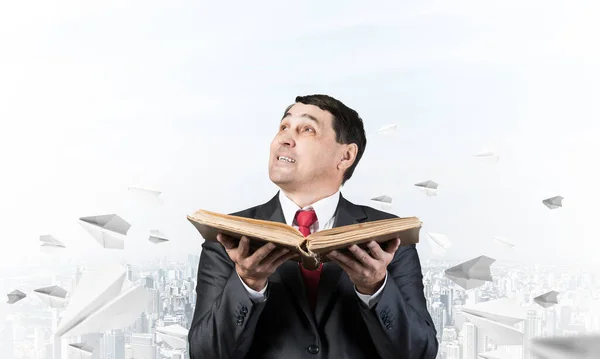Serious businessman with open book looking up