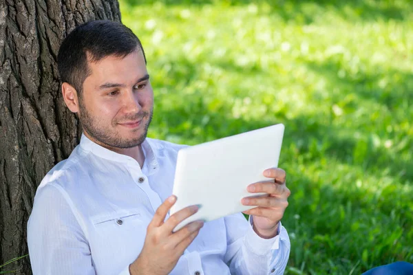 Homem usando tablet computador debaixo da árvore no parque — Fotografia de Stock