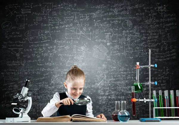 Klein meisje zit aan het bureau met vergrootglas — Stockfoto