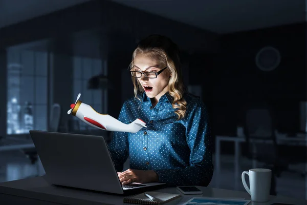 Приваблива блондинка носить окуляри в темному офісі за допомогою ноутбука. Змішані носії — стокове фото