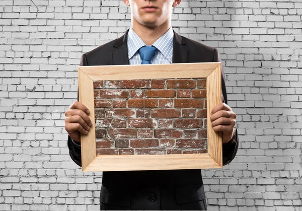 Businessman holding frame with brick texture — Stock Photo, Image