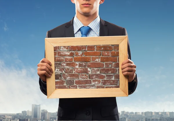 Homme d'affaires tenant le cadre avec la texture de brique — Photo