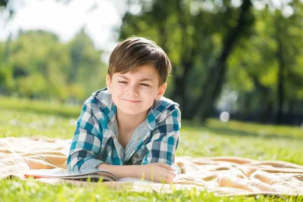 Boy lying on blanket and reading book — Stock Photo, Image