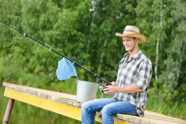 Young man sitting on pier with rod — Stock Photo, Image