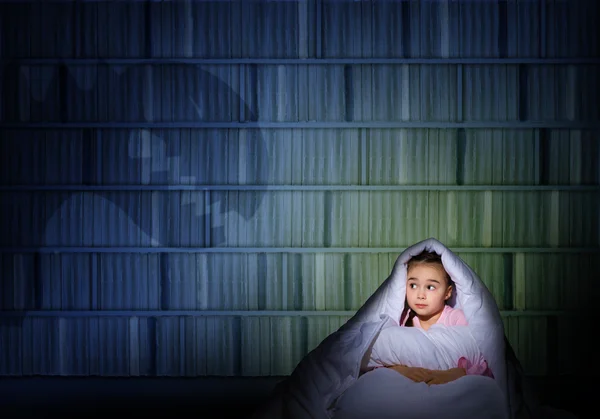 Flicka under täcket med en ficklampa — Stockfoto
