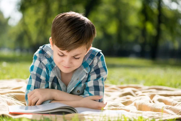 Jongen liggend op deken en lezen van boek — Stockfoto