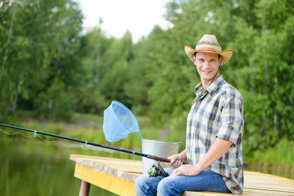 Mladý muž sedí na molu s tyčinkou — Stock fotografie