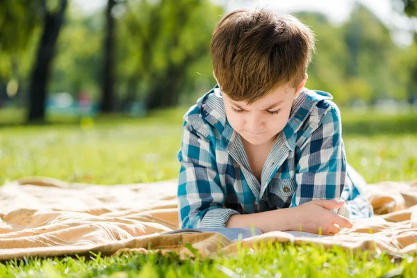 Boy lying on blanket and reading book — Stock Photo, Image