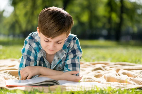 Garçon couché sur couverture et livre de lecture — Photo