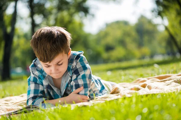 Garçon couché sur couverture et livre de lecture — Photo