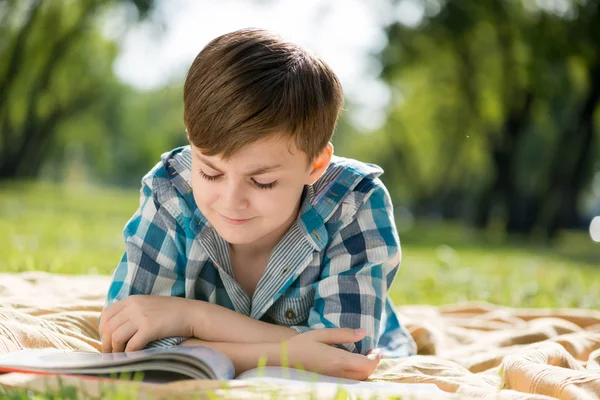 Мальчик лежит на одеяле и читает книгу — стоковое фото