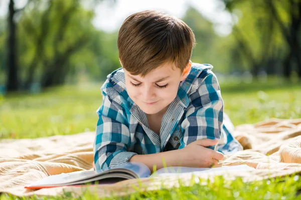 Garçon couché sur couverture et livre de lecture — Photo