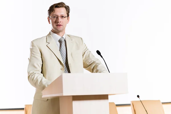 Speaker stands behind a podium — Stock Photo, Image