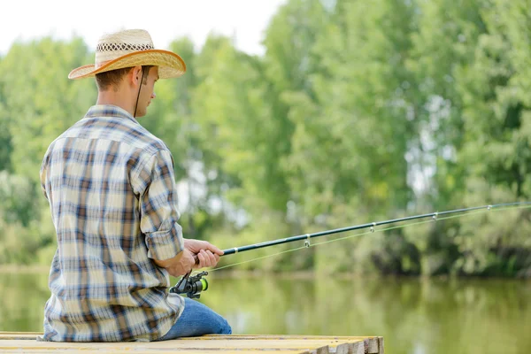 Young man sitting on pier with rod — Stock Photo, Image