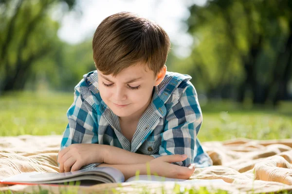 Boy lying on blanket and reading book — Stock Photo, Image