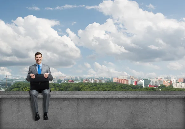 Businessman with suitcase sitting on roof — Stock Photo, Image