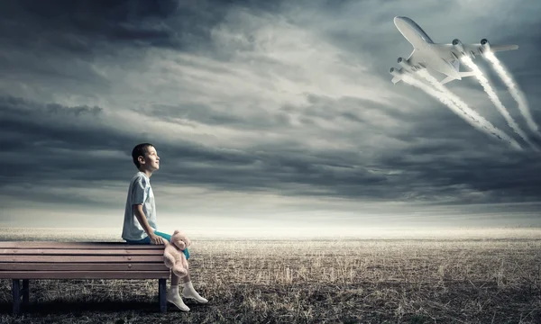 Niño en el banco y avión en el cielo —  Fotos de Stock