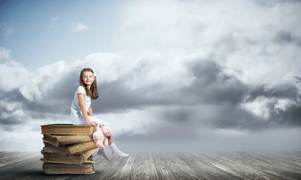 Meisje zit op stapel boeken — Stockfoto