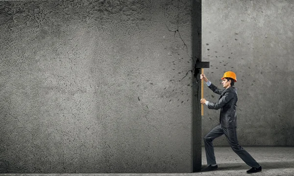 Hombre de negocios en casco rompiendo muro de cemento —  Fotos de Stock