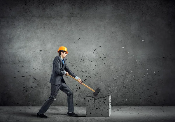 Biznesmen w kasku łamanie cementowe ściany — Zdjęcie stockowe