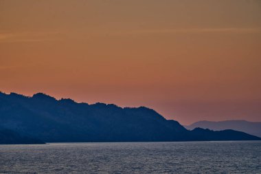 Bukhtarma Barajı 'nın engebeli dağ sırtlarının ardında batan güneşin çarpıcı bir görüntüsü. Görüntü, parlak turuncu bir gökyüzünü su yüzeyine yansıtıyor ve karanlık dağ siluetleri yaratıp, zirveyi yakalıyor.