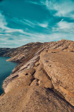 Doğu Kazakistan 'daki Sibinskiye Gölleri' nin çarpıcı yüksek açılı panoramik manzarası. Görüntü, eşsiz, engebeli granit dağ sırtları ve bulutlu gökyüzünün altındaki kaya oluşumları arasında yuva yapmış birkaç derin mavi göl sergiliyor.