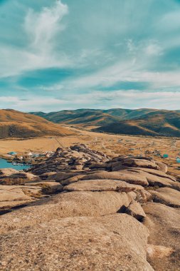 Doğu Kazakistan 'daki Sibinskiye Gölleri' nin çarpıcı yüksek açılı panoramik manzarası. Görüntü, eşsiz, engebeli granit dağ sırtları ve bulutlu gökyüzünün altındaki kaya oluşumları arasında yuva yapmış birkaç derin mavi göl sergiliyor.