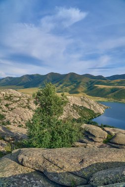 Doğu Kazakistan 'daki Sibinskiye Gölleri' nin çarpıcı yüksek açılı panoramik manzarası. Görüntü, eşsiz, engebeli granit dağ sırtları ve bulutlu gökyüzünün altındaki kaya oluşumları arasında yuva yapmış birkaç derin mavi göl sergiliyor.