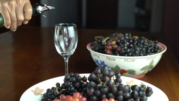 人は赤ワインを木のテーブルの上のワイングラスに注ぎ 収穫したばかりのブドウをセラミックプレートとボウルに入れます — ストック動画