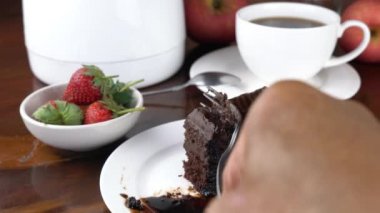 Seramik tabakta lezzetli çikolatalı pasta yemek. Metal çatal kullanan adam çikolata soslu çikolatalı pastadan bir ısırık alıyor..