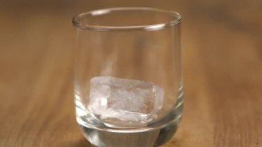 Tahta masadaki bir bardağa buz küpü at. Barmen buzları bardağa koyup buzlu viski hazırlıyor..