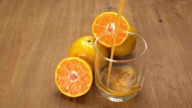 Portakal suyunu portakallı bir bardağa döküyor ve ahşap bir masaya yarımlar döküyor..