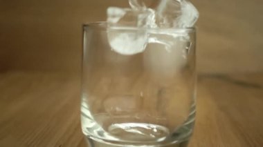 Buz küplerini şeffaf bir bardağa, ahşap masanın üzerine yavaş çekimde atmak. Barmen viski koymadan önce bardağa buz koyuyor..