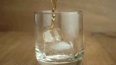 Ağır çekimde ahşap masaya buz küpleriyle dolu bardağa viski dökerek. Viski ağır çekimde buzlu cama dökülüyor..