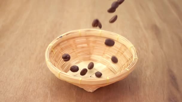 スローモーションで木製のテーブルの上に竹のバスケットに落ちる焙煎コーヒー豆 香り高いコーヒーの種が落ち — ストック動画