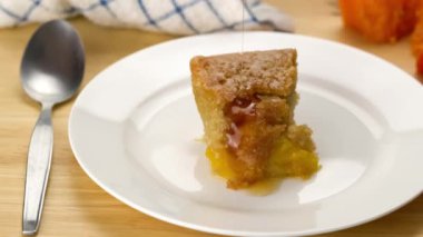 Tahta masadaki beyaz seramik tabakta taze meyveli kekin üzerine bal dökmek. Tahta masadaki ballı taze mango meyveli pasta manzarası