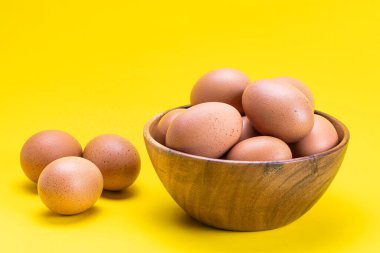 Tahta kasede taze tavuk yumurtaları ve kırpma yolu ile sarı arka planda.