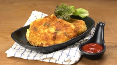 Şef, jambonlu peynirli kroket parçalarını küçük siyah bardakta ketçapla siyah bir tabağa koydu. Jambon peynirli kroket, jambon ve peynirle doldurulmuş kızarmış patates püresidir..