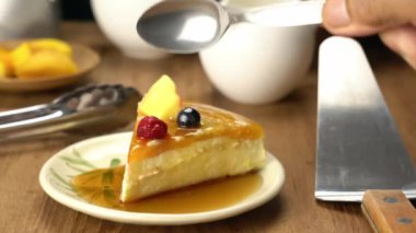 Sunbae metal kaşık kullanarak lezzetli ev yapımı mango peynirli kekten bir ısırık alıyor. Olgun mango, ahududu ve seramik tabağa bal dökülüyor..