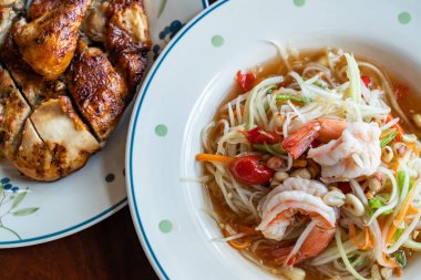 Beyaz seramik tabakta karides ve ahşap masada kızarmış tavuk ile nefis yeşil papaya salatası manzarası..