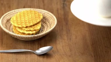 Yaşlı adam beyaz seramik bir fincan sıcak sütlü kahveyi ahşap masaya koyuyor bambu tepsisinde çıtır çıtır waffle ve metal bir kaşık..