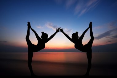 Kadınlar gün batımında yoga yapıyor.