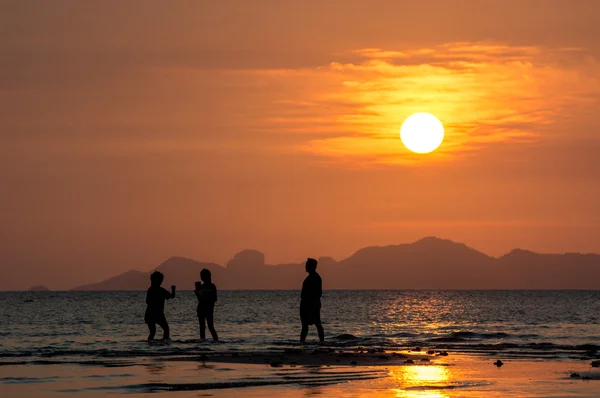 Sylwetki ludzi na plaży o zachodzie słońca — Zdjęcie stockowe