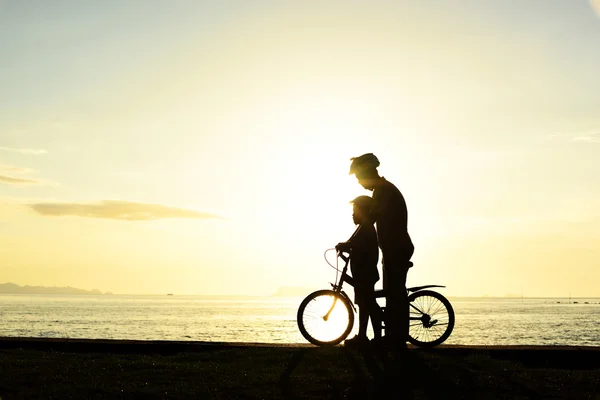 Far och pojke med cykel på stranden — Stockfoto