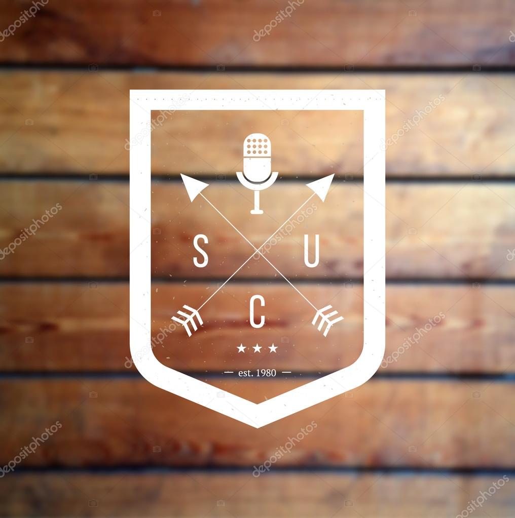 Hipster vector logo shield with crossed arrows and retro mic at blurred wooden background