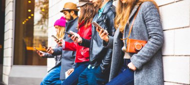 Bir grup arkadaş cep telefonlarında uygulama kullanıyor. Teknolojiye bağımlı hippiler. Gençlik, sosyal ve arkadaşlık kavramı. Bir grup çok ırklı arkadaş akıllı cep telefonlarını izliyor ve selfie çekiyor..