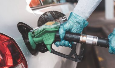 Yeni arabasına benzin dolduran bir kadın. Salgın sırasında benzin fiyatları düşüyor. Benzin istasyonunda araba dolduran bir tüketici. Benzin ve mazot dolum istasyonu. Kadın eldiven takıyor.