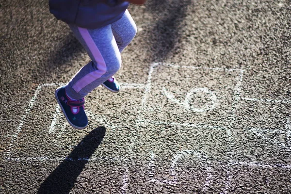 Kid playing hopscotch on playground outdoors. Little children playing hopscotch drawn with colorful chalk on asphalt Closeup of little boy\'s legs and hopscotch drawn on asphalt Child playing hopscotch